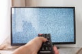 Hand with TV remote control in front of the screen with white noise on it - tuning the television channels and connecting problems Royalty Free Stock Photo