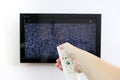 Hand with TV remote control in front of the screen with white noise on it - tuning the television channels and Royalty Free Stock Photo