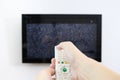 Hand with TV remote control in front of the screen with white noise on it - tuning the television channels and connecting problems Royalty Free Stock Photo