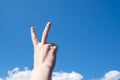 Hand with two fingers up in the symbol of peace or victory. Isolated on blue sky background with clouds, copy space Royalty Free Stock Photo