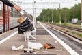 Hand of unknown man throws trash into overcrowded trash basket on a railway platform. Garbage bin