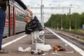 Hand of unknown man throws trash into overcrowded trash basket on a railway platform. Garbage bin