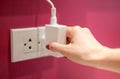 Hand is unplug the electric line off a white socket on the red wall