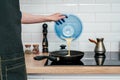 Hand of unrecognizable man in black apron pouring omelette mix from blue plastic bowl in frying pan on electric cooker. Royalty Free Stock Photo