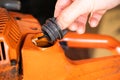 A hand unscrews the cap of the fuel mixture tank in an orange chainsaw. Gas tank for gasoline of a two-stroke engine close-up.