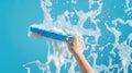 A hand using a blue squeegee to clean a soapy surface against a bright blue background Royalty Free Stock Photo