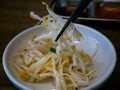 Hand using chopsticks pick Korean seasoned beansprout Mild kongnamul muchim in a white cup for eating