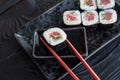 Hand using chopsticks pick. Maki-Sushi, tuna-maki rolls on a black stone plate. Fresh made Sushi set with tuna, cheese and cucumbe Royalty Free Stock Photo