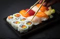 Hand using chopsticks pick Sushi and Sashimi rolls on a black stone slatter. Fresh made Sushi set with salmon, prawns, wasabi and Royalty Free Stock Photo