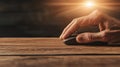 Hand using computer mouse on wooden desk with bright light overhead, representing freelance work and digital tasks. Royalty Free Stock Photo