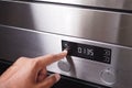 A hand is using a finger to activate the timer button on the control panel of a stainless steel oven