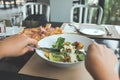 A hand using fork and knife to eat Ceasar salad with pizza on dining table Royalty Free Stock Photo