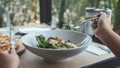 A hand using fork to scoop up Ceasar salad to eat with pizza on dining table Royalty Free Stock Photo