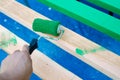 Hand using 6 inches paint roller for first coat of latex paint on 2 by 4 wooden boards on sawhorse with blue tarp cover paint Royalty Free Stock Photo