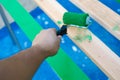 Hand using 6 inches paint roller for first coat of latex paint on 2 by 4 wooden boards on sawhorse with blue tarp cover paint Royalty Free Stock Photo