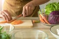 Hand is using knife cutting carrots and have a purple cauliflower cup in to next to it. The preparation for the vegetable salad