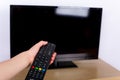 Hand using a remote control to turn off on on the TV with an empty screen