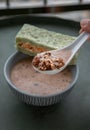 Hand using spoon picking up malt flakes granola in almond milk served with sandwich on ceramic bowl