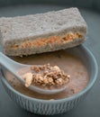 Hand using spoon picking up malt flakes granola in almond milk served with sandwich on ceramic bowl