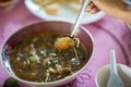 Hand is using a spoon to scoop Chinese style soup; or braised fish maw in red gravy with eggs, mushroom, and bamboo shoot in white Royalty Free Stock Photo