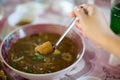 Hand is using a spoon to scoop Chinese style soup; or braised fish maw in red gravy with eggs, mushroom, and bamboo shoot in white Royalty Free Stock Photo