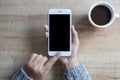 Hand using white smart phone black screen on top view, with white coffee cup on wooden table Royalty Free Stock Photo