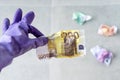 Hand in violet rubber gloves for cleaning holding crumpled euro bills on a gray background. Payment for work, trash money, Royalty Free Stock Photo