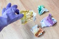 Hand in violet rubber gloves for cleaning holding crumpled euro bills on a wooden background. Payment for work, trash money, Royalty Free Stock Photo