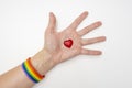 A hand wearing lgbt rainbow bracelet and red heart lying on an open palm