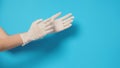 The hand is wearing white surgical gloves or latex gloves on a blue or Turquoise background