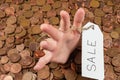 The hand which is sticking out of heap of coins with sales tag.Copy space