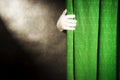 Hand in white glove on a background of green curtains, with the light from the reflector on a black background