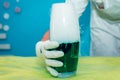 A hand in a white glove holds a vessel with green liquid and steam