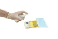 A hand in a white glove is processing an antiseptic of a banknote of 200 two hundred euros, next to a blue medical mask. The conce