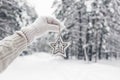 A hand in white mittens and a sweater holds a carved wooden star