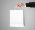 Hand in white shirt and black jacket holds a white gift bag Royalty Free Stock Photo