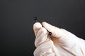 Hand in a white sterile glove holds a piercing for cartilage ear jewelry on a dark background close-up