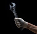 A hand in a white work glove holds a large locksmith\'s adjustable wrench on a black background Royalty Free Stock Photo