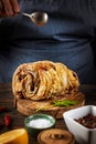 Hand of a woman cook holds a spoon over baked pork with greens on a slate board on a wooden background Royalty Free Stock Photo