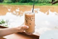 Hand of woman holding glass of iced coffee by riverside Royalty Free Stock Photo