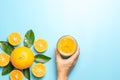 Hand of woman holding glass of orange juice and orange fruits with sliced pieces and leaves on blue background Royalty Free Stock Photo