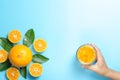 Hand of woman holding glass of orange juice and orange fruits with sliced pieces and leaves on blue background Royalty Free Stock Photo