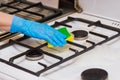 Hand of a woman in a household rubber glove sponges the grate of a gas stove and burners on kitchen, close up Royalty Free Stock Photo