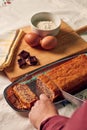 Hand of a woman with a knife cuts a sponge cake with some ingredients on a white tablecloth Royalty Free Stock Photo