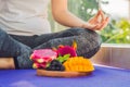 Hand of a woman meditating in a yoga pose, sitting in lotus with fruits in front of her dragon fruit, mango and mulberry