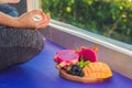 Hand of a woman meditating in a yoga pose, sitting in lotus with fruits in front of her dragon fruit, mango and mulberry