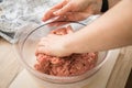 Hand of woman mixing mixed minced meat of pork and beef with ground spices in bowl on cutting board for cooking in domestic