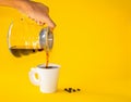 Hand woman pouring coffee on white paper cup with Roasted beans on yellow background Royalty Free Stock Photo