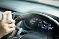 Hand of woman is spraying alcohol,disinfectant spray on steering wheel in her car,prevent infection of Covid-19 virus,