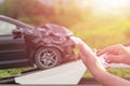 Hand of woman using smartphone and blur of her broken car parking on the road. Contacting car technician, Insurance or need help